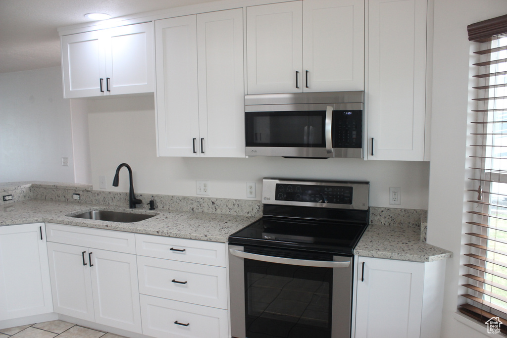 Kitchen featuring light stone counters, a sink, white cabinetry, light tile patterned floors, and stainless steel appliances