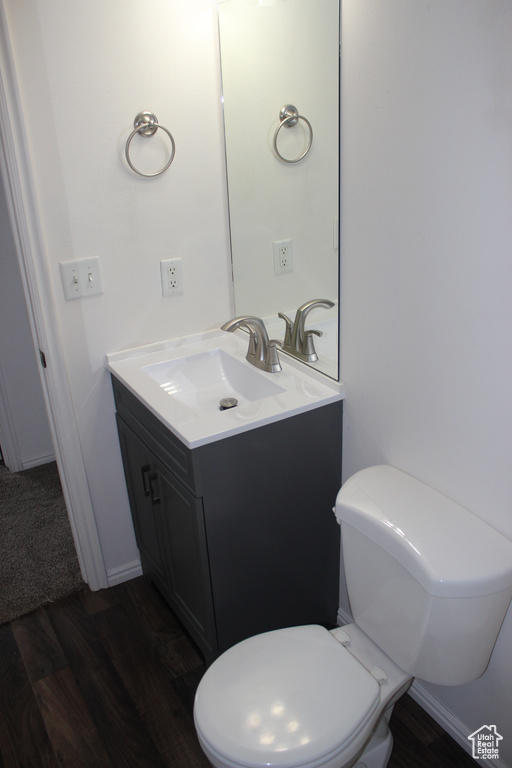 Half bathroom with toilet, wood finished floors, and vanity