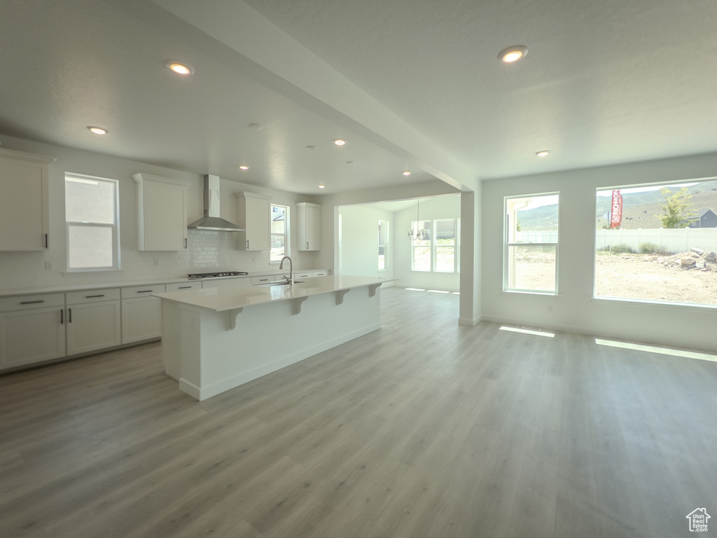 Kitchen with wall chimney range hood, open floor plan, a kitchen island with sink, a breakfast bar area, and recessed lighting