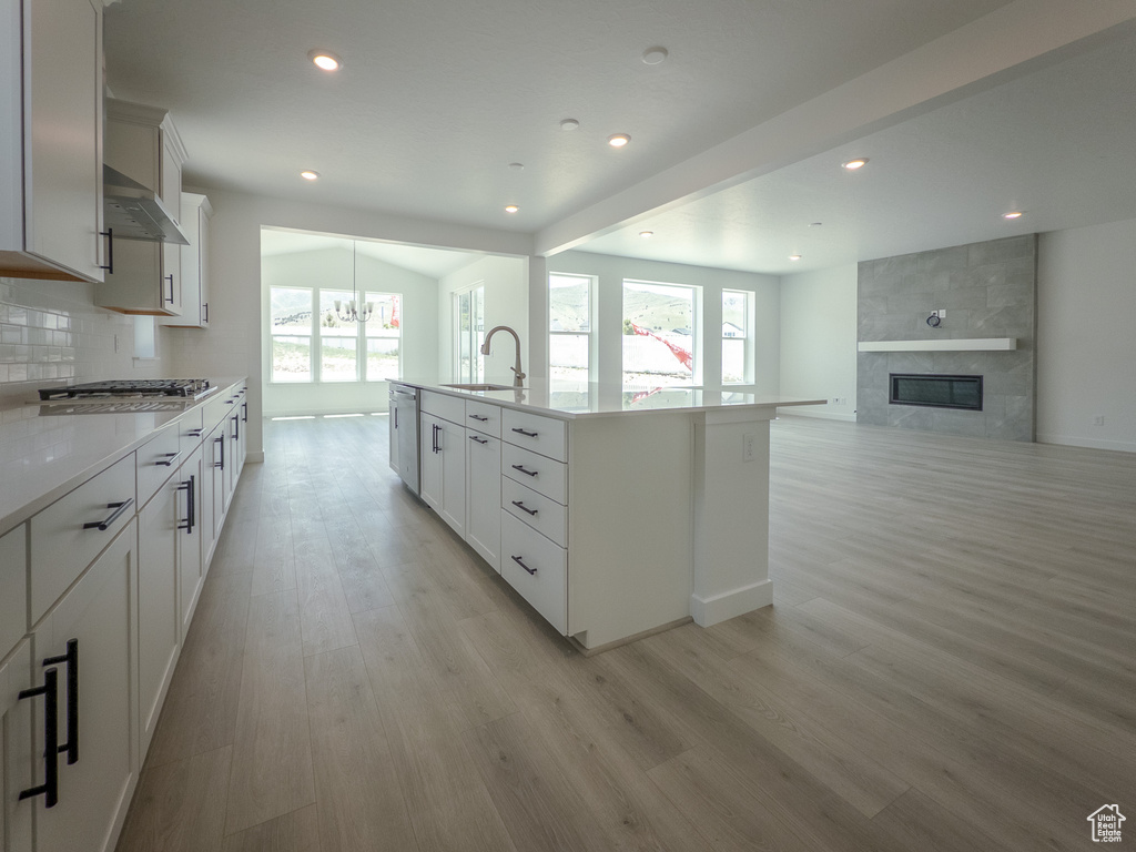 Kitchen with light wood-style floors, stainless steel gas stovetop, light countertops, recessed lighting, and a tile fireplace
