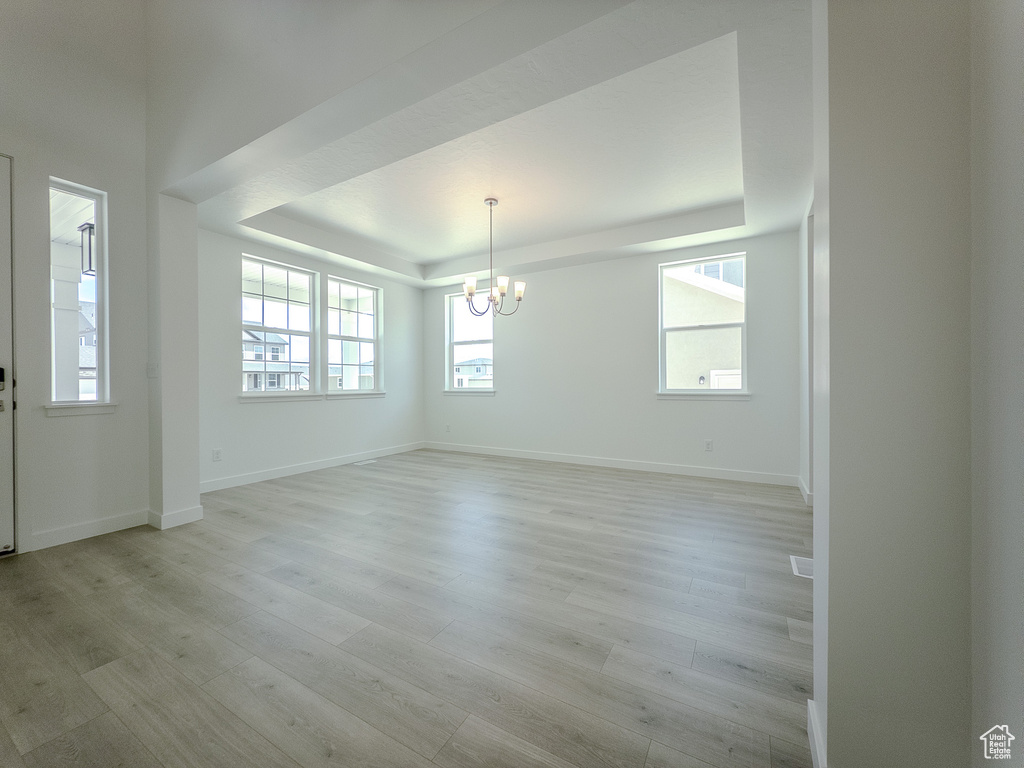 Spare room featuring a raised ceiling, a chandelier, light wood-type flooring, and baseboards