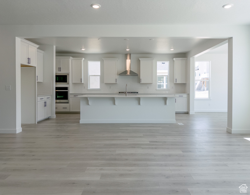 Kitchen with appliances with stainless steel finishes, wall chimney range hood, a sink, a breakfast bar area, and light countertops