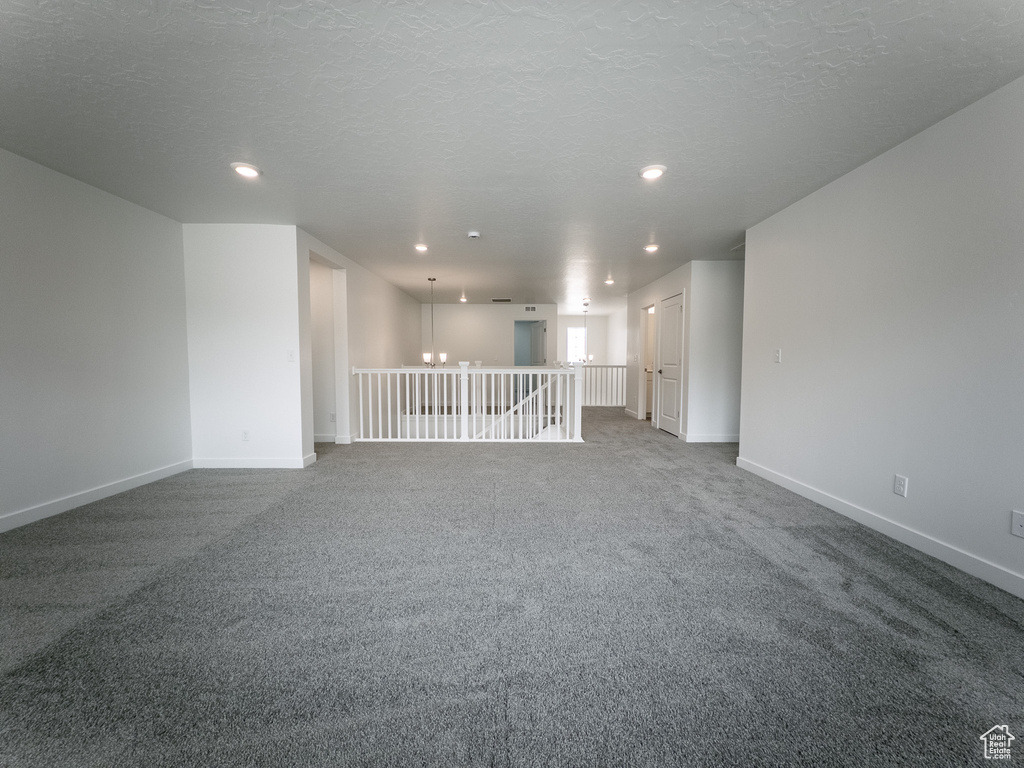Spare room featuring dark carpet, baseboards, recessed lighting, a chandelier, and a textured ceiling