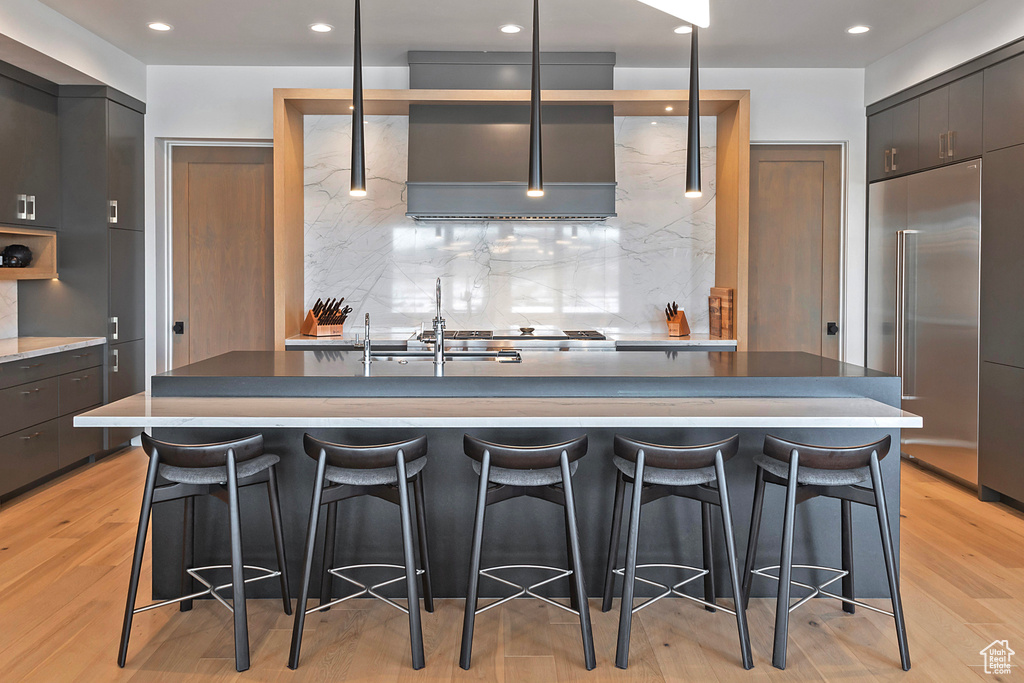 Kitchen with built in refrigerator, modern cabinets, decorative backsplash, a breakfast bar, and light wood-type flooring