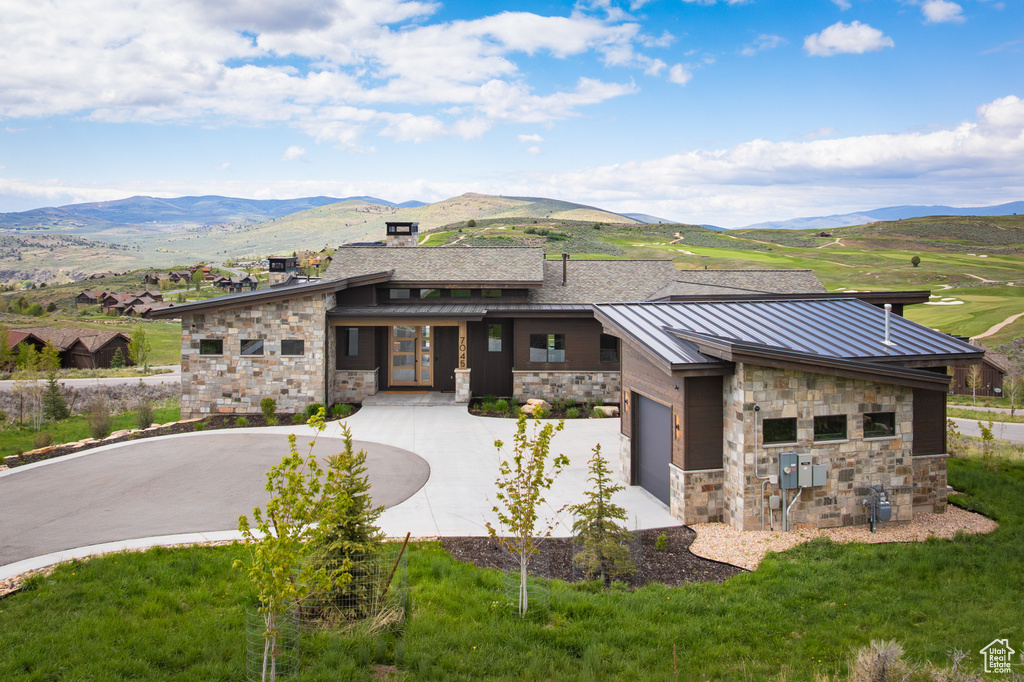 View of front of home with stone siding, a standing seam roof, curved driveway, a mountain view, and metal roof