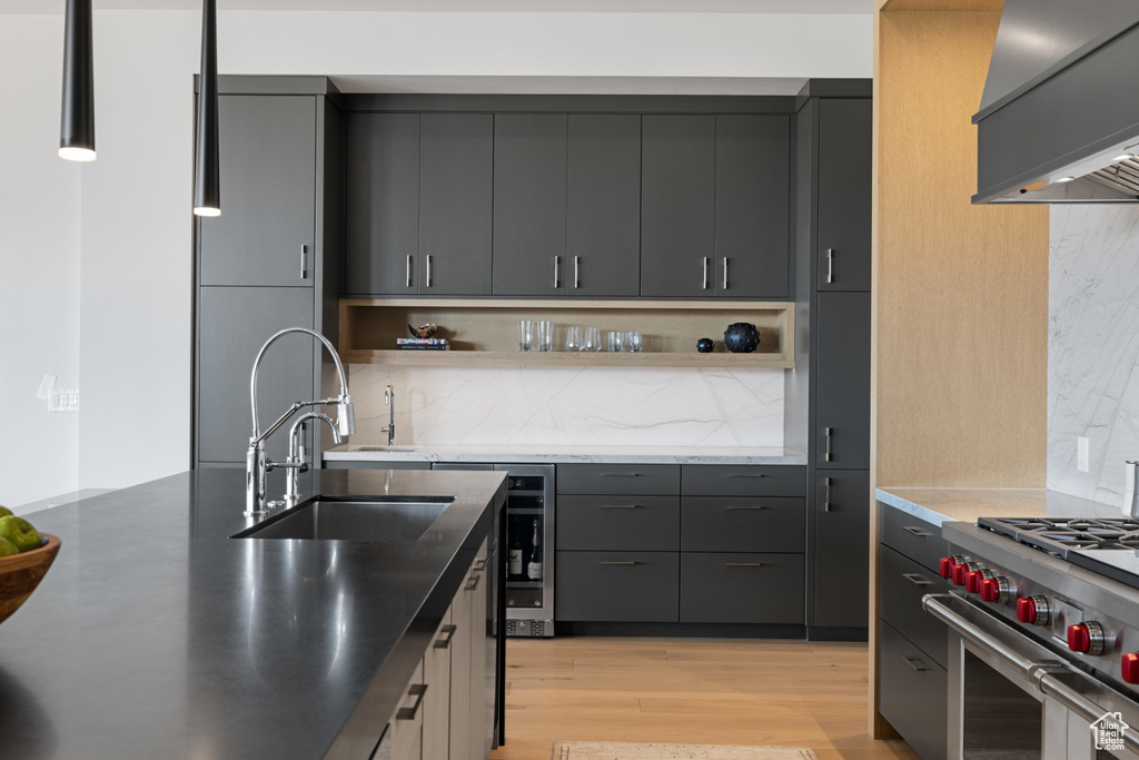 Kitchen with open shelves, wall chimney exhaust hood, a sink, high end stainless steel range oven, and light wood finished floors