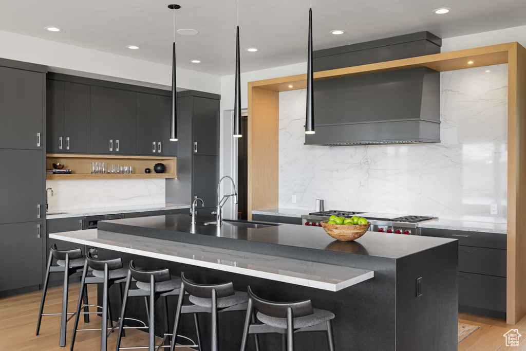 Kitchen featuring open shelves, a sink, an island with sink, backsplash, and a breakfast bar