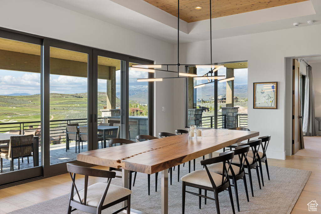Dining room with a raised ceiling, light wood-style floors, wood ceiling, a chandelier, and view of golf course