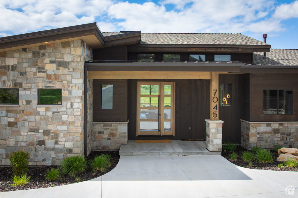 Property entrance featuring stone siding, a porch, and roof with shingles