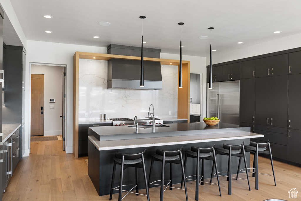 Kitchen with built in refrigerator, dark cabinets, a kitchen bar, decorative backsplash, and recessed lighting