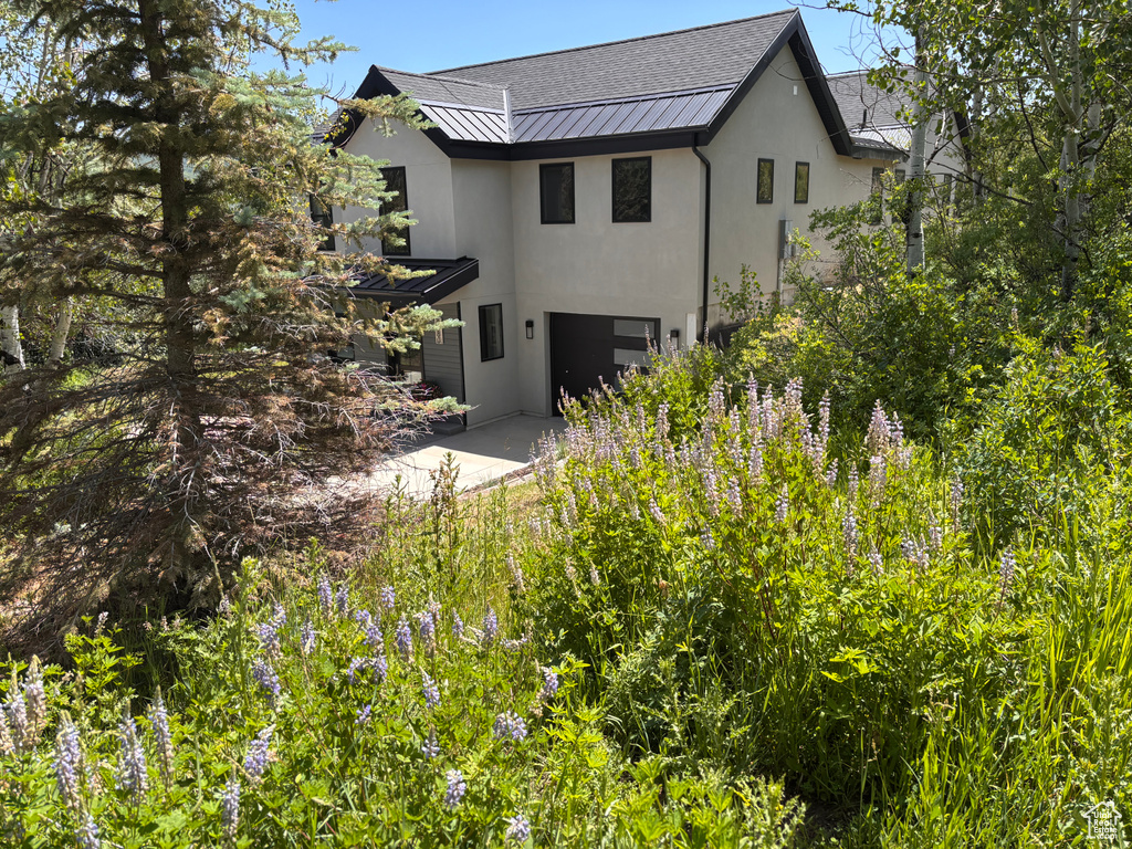 Rear view of property with a standing seam roof, stucco siding, a garage, and a metal roof
