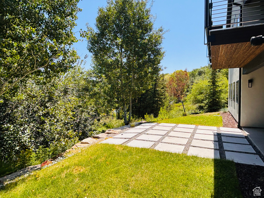 View of green lawn with a patio and a balcony