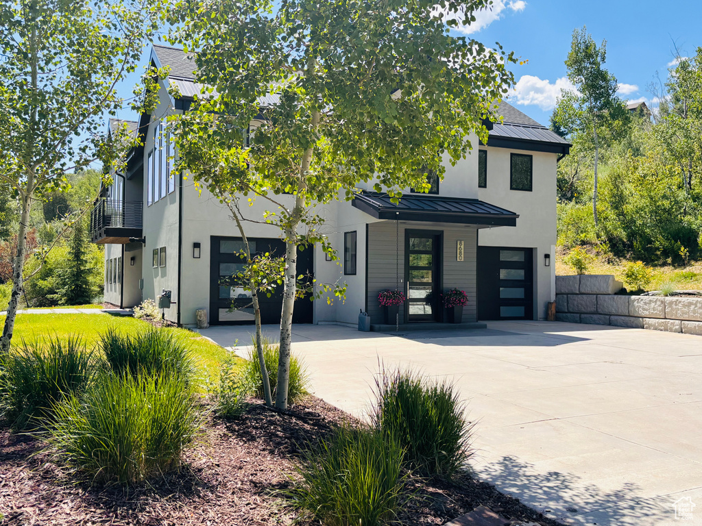 View of front facade featuring a standing seam roof, driveway, and stucco siding