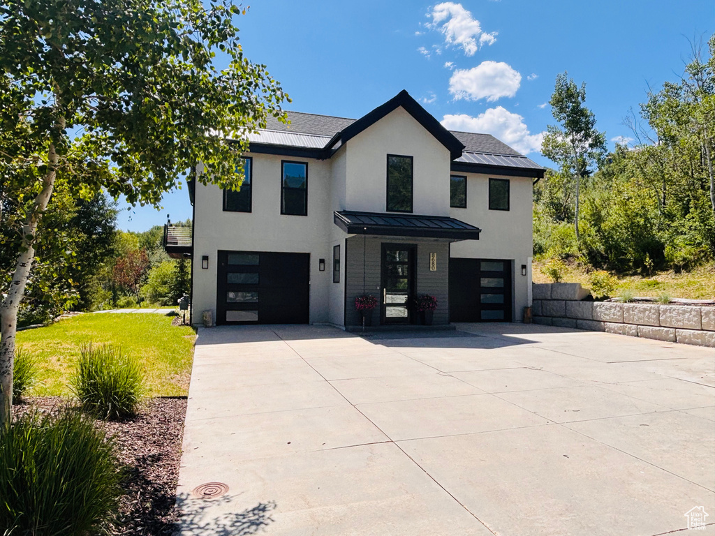 Modern farmhouse featuring an attached garage, concrete driveway, a standing seam roof, a front lawn, and a metal roof