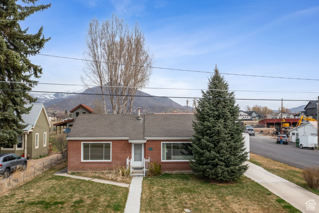 View of front facade featuring fence, a mountain view, a front lawn, brick siding, and a shingled roof