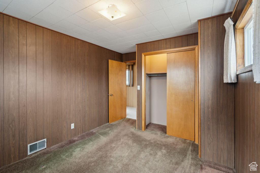 Unfurnished bedroom featuring a closet, carpet floors, visible vents, and wood walls