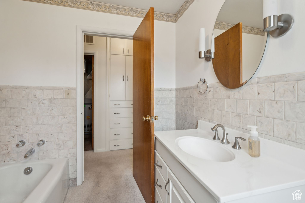 Full bath featuring vanity, a tub to relax in, tile walls, and wainscoting