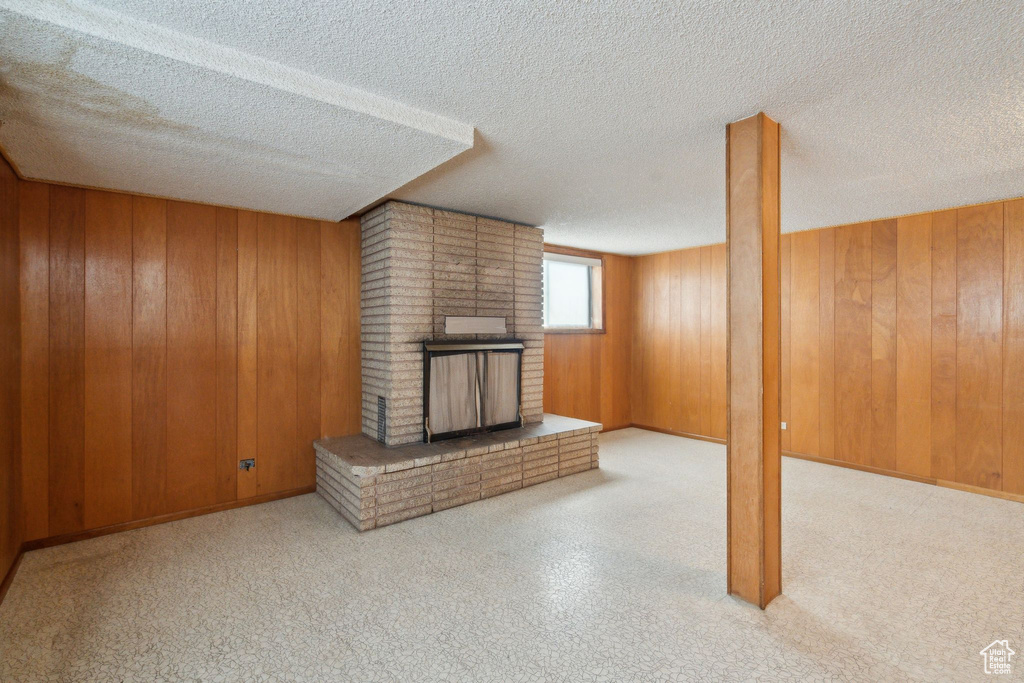 Unfurnished living room with a brick fireplace, wood walls, baseboards, and a textured ceiling