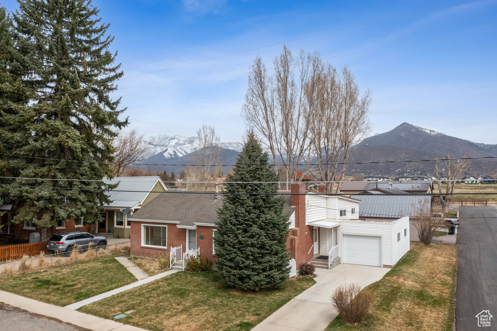 View of front of house with fence, brick siding, a front lawn, driveway, and a mountain view