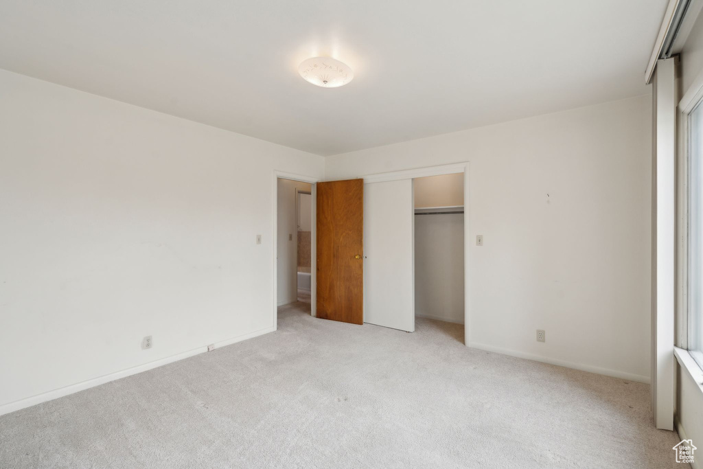 Unfurnished bedroom featuring light colored carpet, a closet, and baseboards