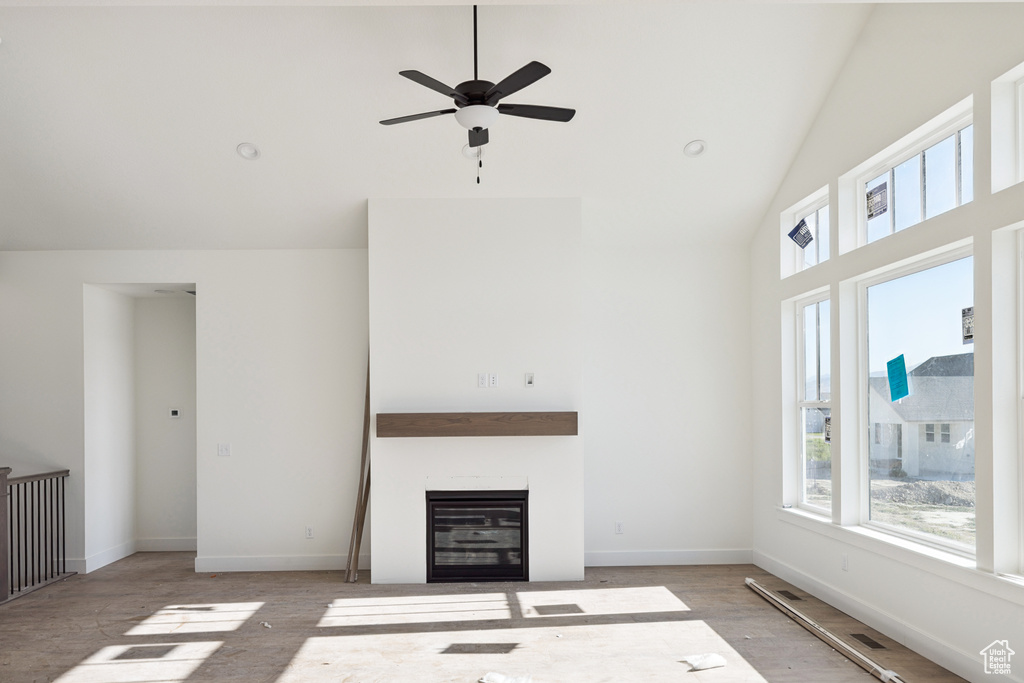 Unfurnished living room with high vaulted ceiling, plenty of natural light, ceiling fan, a glass covered fireplace, and wood finished floors