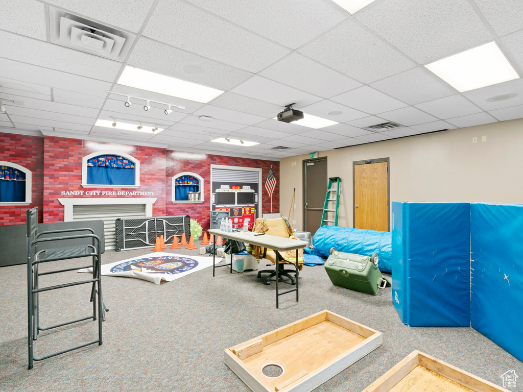 Recreation room with a drop ceiling, brick wall, a fireplace, and visible vents