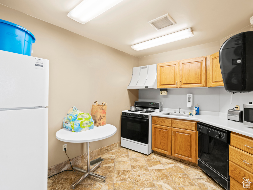 Kitchen with black dishwasher, a sink, freestanding refrigerator, exhaust hood, and gas range