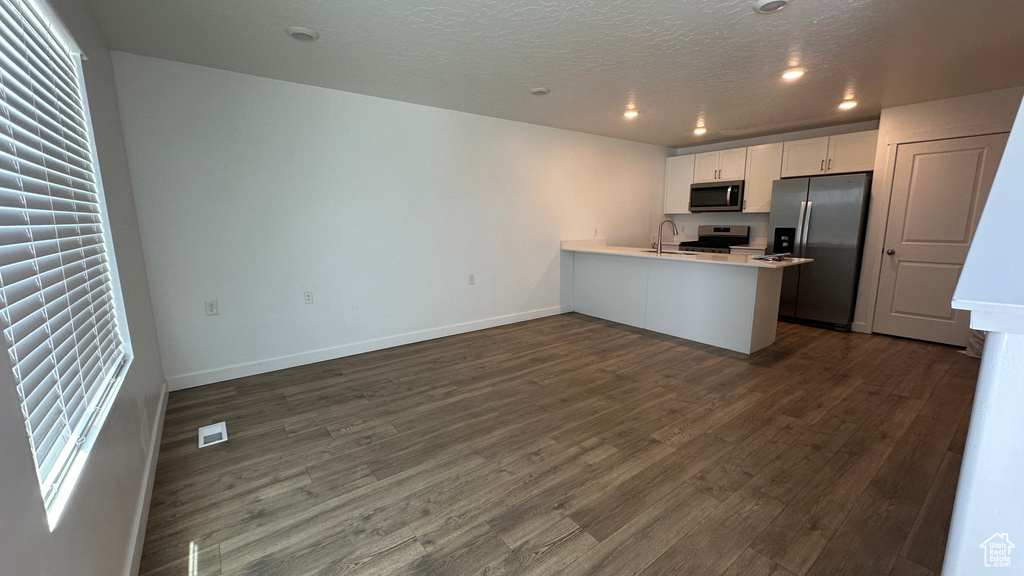Kitchen with dark wood finished floors, a sink, white cabinets, a peninsula, and appliances with stainless steel finishes