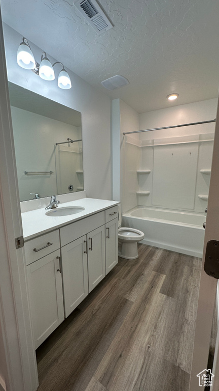 Bathroom with a textured ceiling, visible vents, wood finished floors, toilet, and vanity
