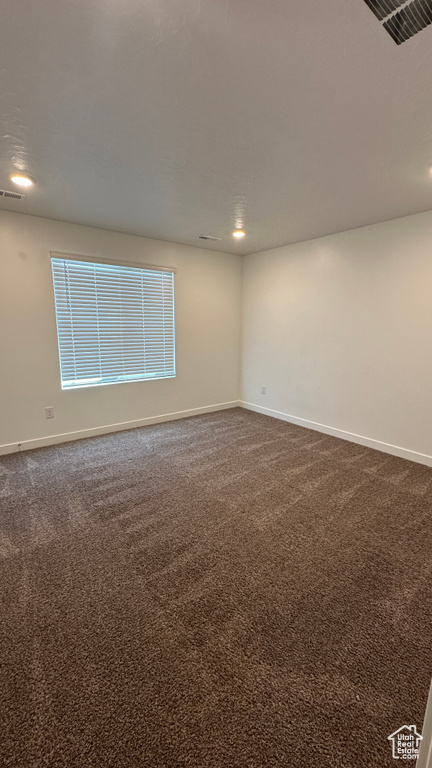 Spare room with baseboards, visible vents, and dark colored carpet
