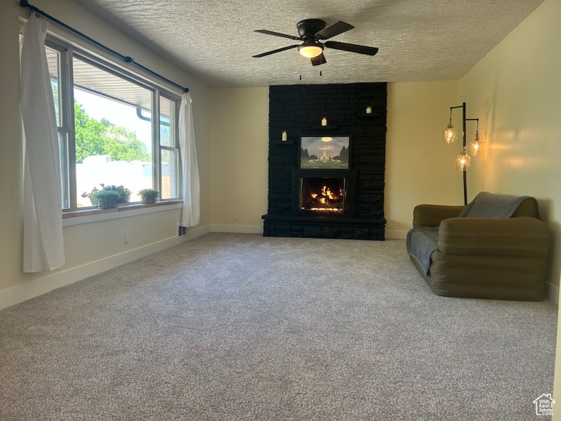 Living area featuring a ceiling fan, a textured ceiling, a large fireplace, and carpet