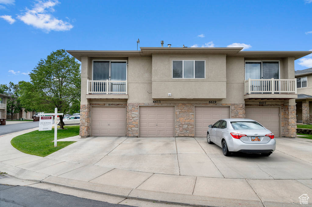 View of property with an attached garage, stone siding, stucco siding, and driveway