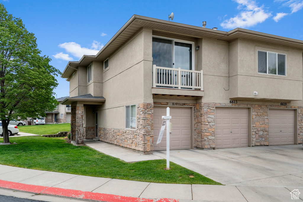 View of front facade featuring stone siding, an attached garage, a front lawn, stucco siding, and a balcony