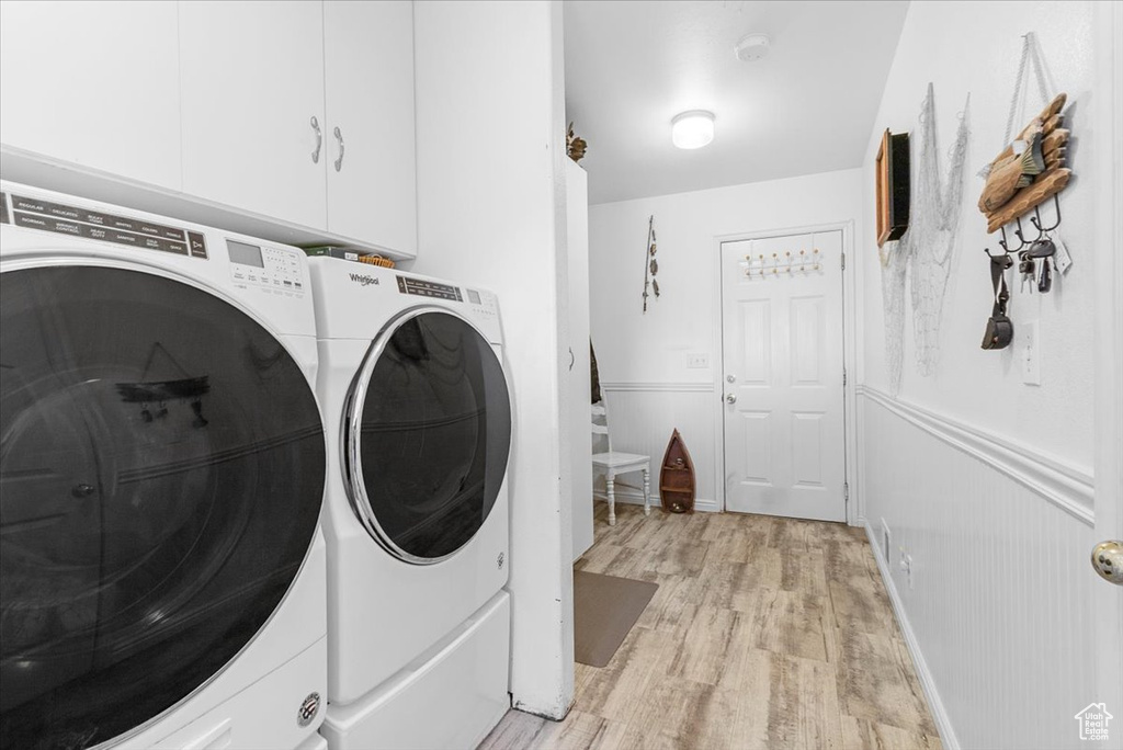 Washroom featuring light wood finished floors, cabinet space, separate washer and dryer, and wainscoting