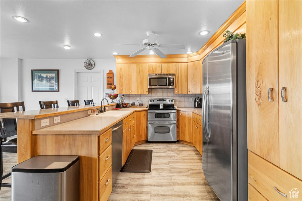 Kitchen featuring a peninsula, a breakfast bar, stainless steel appliances, a sink, and backsplash