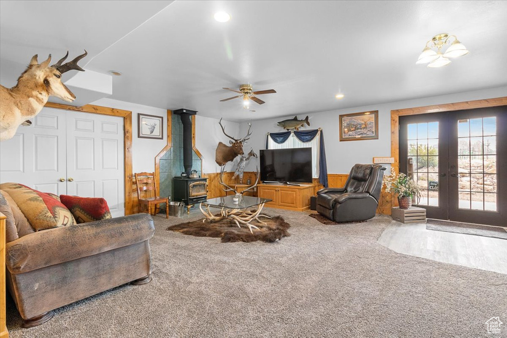 Carpeted living room with french doors, ceiling fan, recessed lighting, a wood stove, and wainscoting