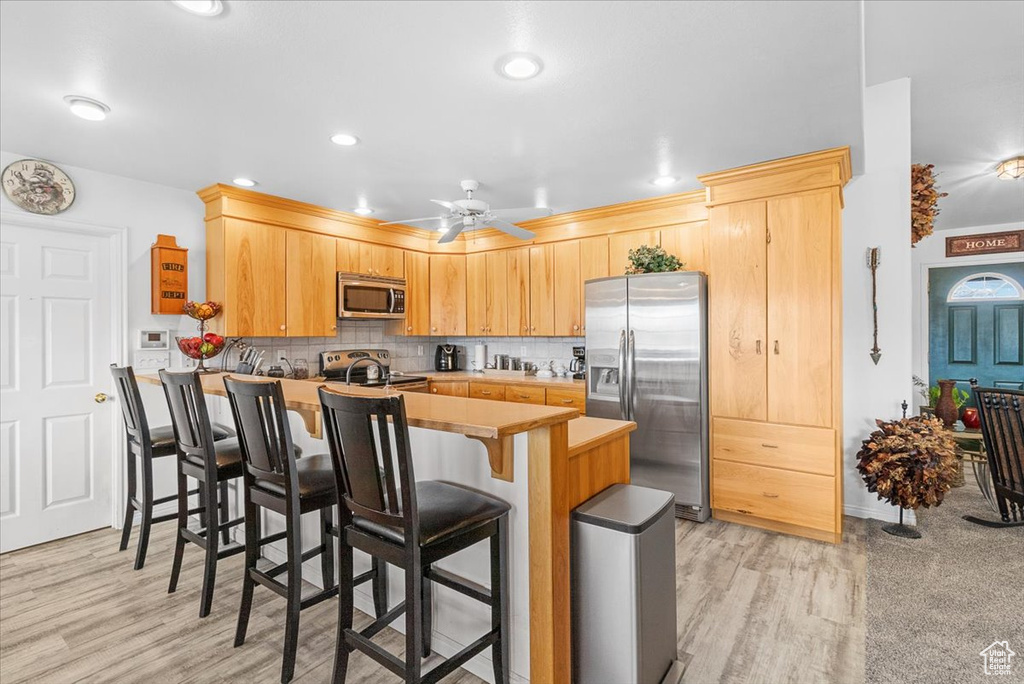 Kitchen featuring decorative backsplash, a peninsula, ceiling fan, stainless steel appliances, and a breakfast bar area