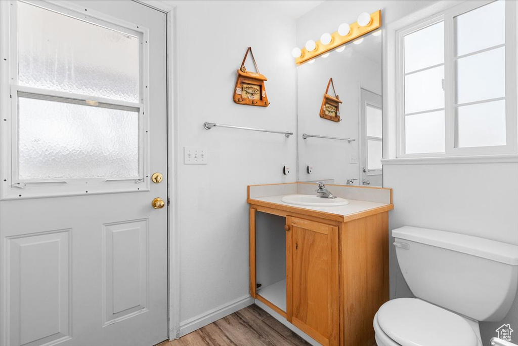 Half bath with baseboards, toilet, vanity, and wood finished floors