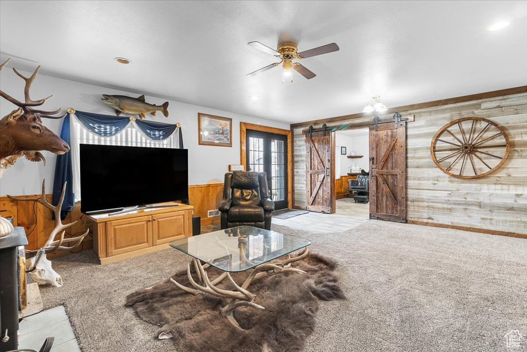 Living area featuring wooden walls, a barn door, light colored carpet, and ceiling fan