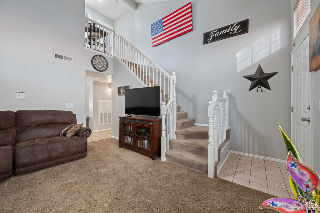 Carpeted living area with stairway, baseboards, tile patterned floors, a towering ceiling, and visible vents
