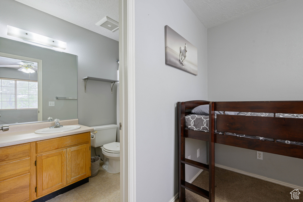 Bathroom featuring vanity, toilet, baseboards, a textured ceiling, and a ceiling fan