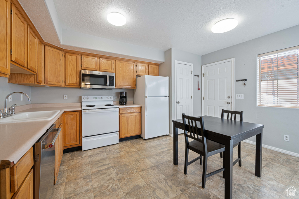 Kitchen with light countertops, a sink, a textured ceiling, stainless steel appliances, and baseboards