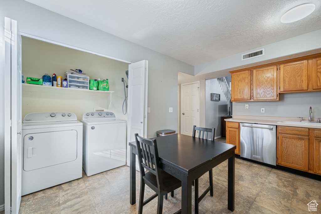 Kitchen featuring light countertops, separate washer and dryer, stainless steel dishwasher, a sink, and visible vents