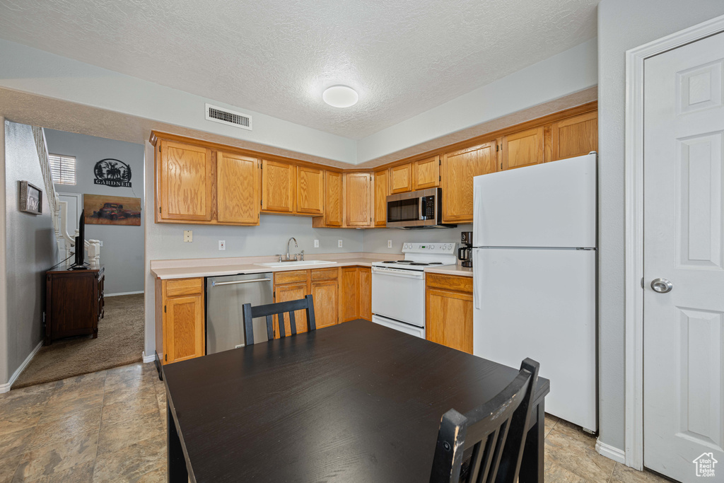 Kitchen with light countertops, a sink, a textured ceiling, stainless steel appliances, and baseboards