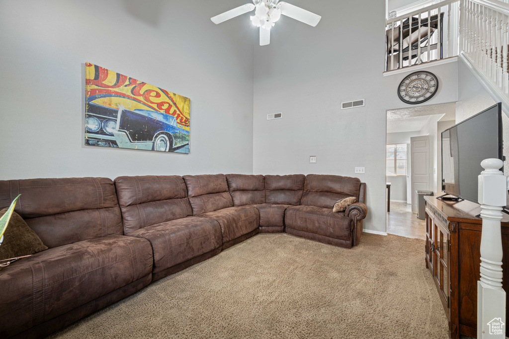 Living area featuring carpet flooring, a ceiling fan, a high ceiling, and visible vents