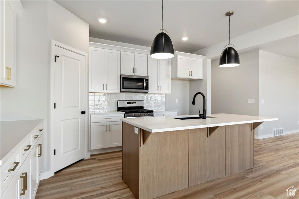 Kitchen with backsplash, a sink, light wood-style flooring, stainless steel appliances, and a kitchen island with sink