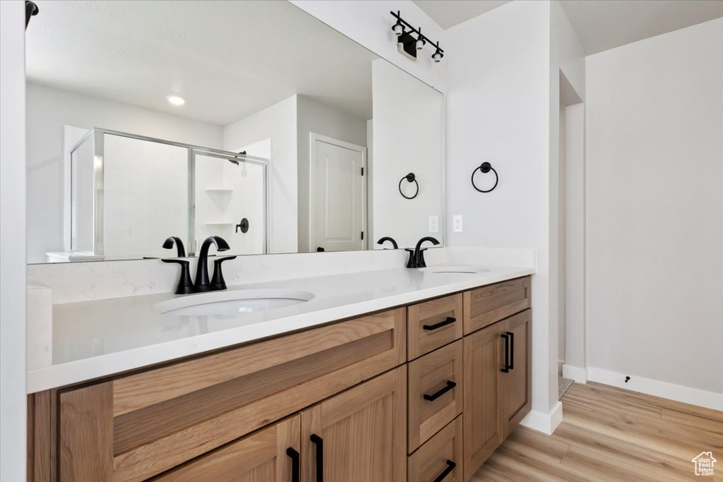 Bathroom featuring double vanity, a sink, a stall shower, and wood finished floors