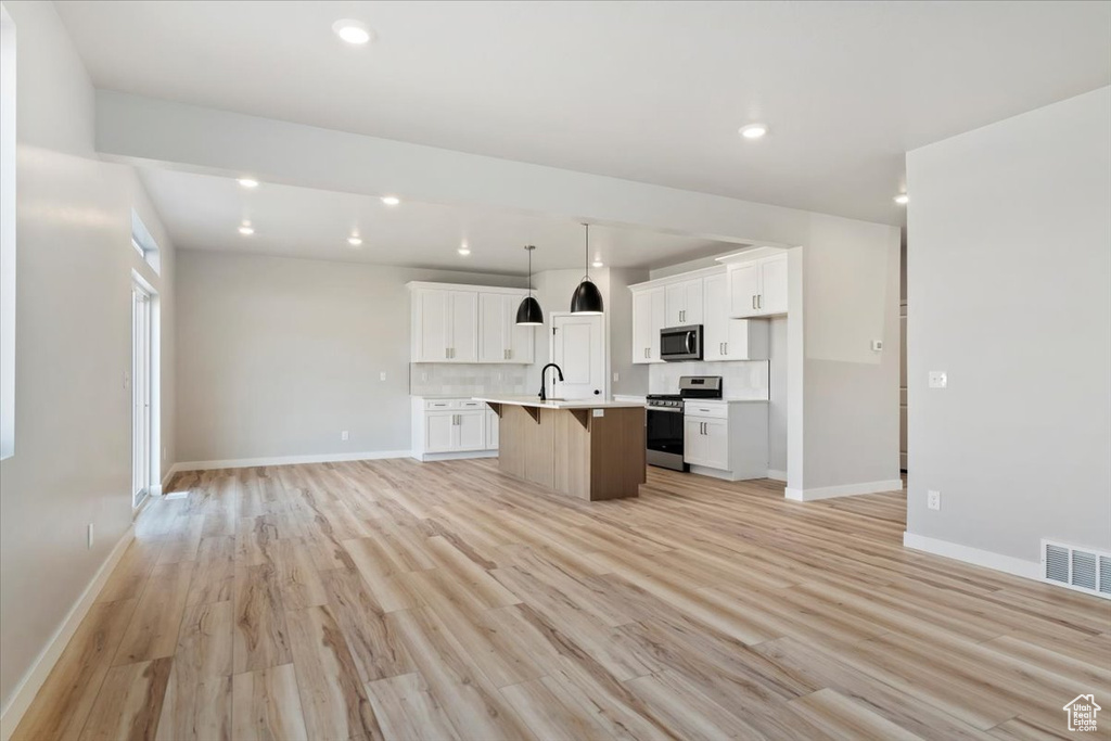 Kitchen with open floor plan, stainless steel appliances, a sink, visible vents, and a kitchen island with sink