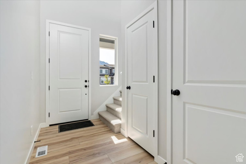 Foyer with light wood finished floors, baseboards, visible vents, and stairs