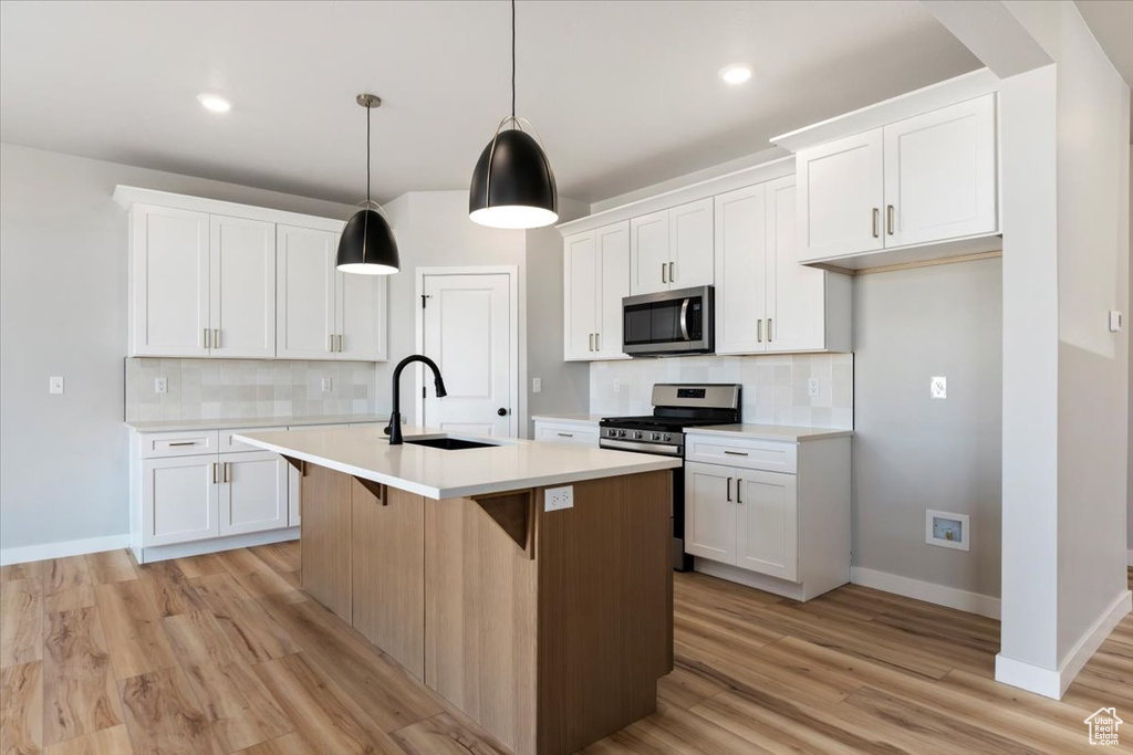 Kitchen with light countertops, a sink, stainless steel appliances, and an island with sink